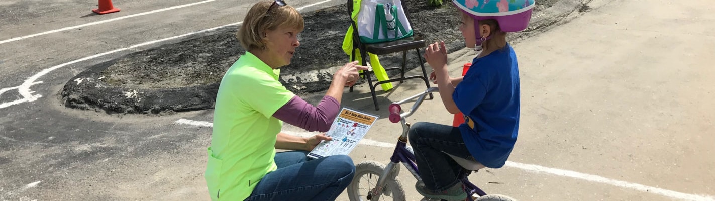Woman kneels down to young girl on bike to teach bike safety image
