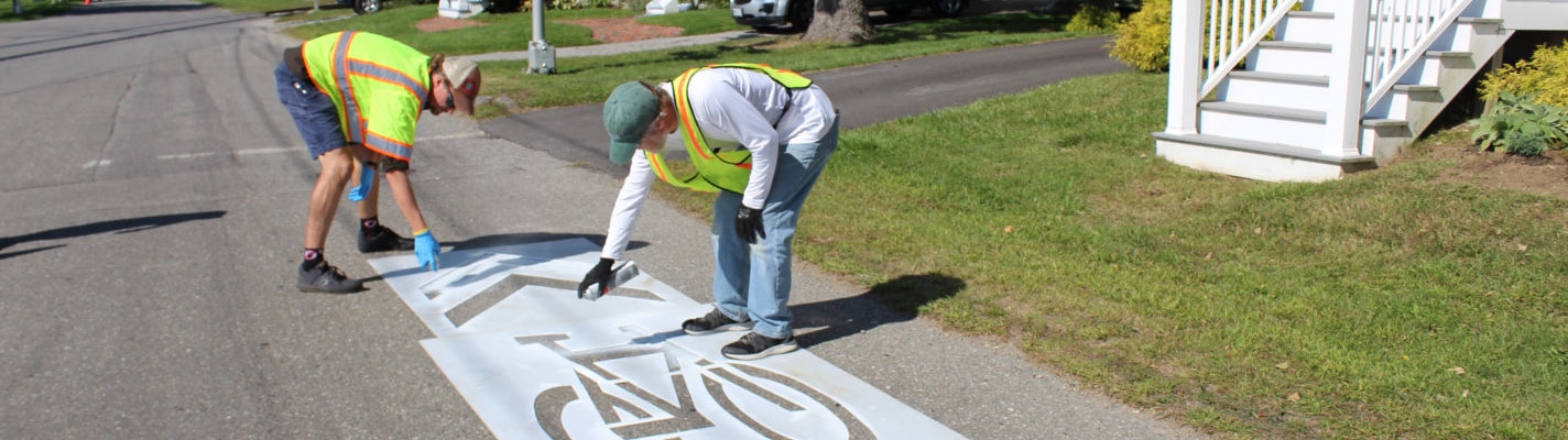 Twp people use stencil to paint bike sharrow on road image