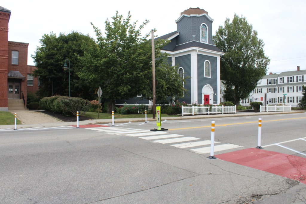 Crosswalk enhanced by paint, bollards, and no parking zones.