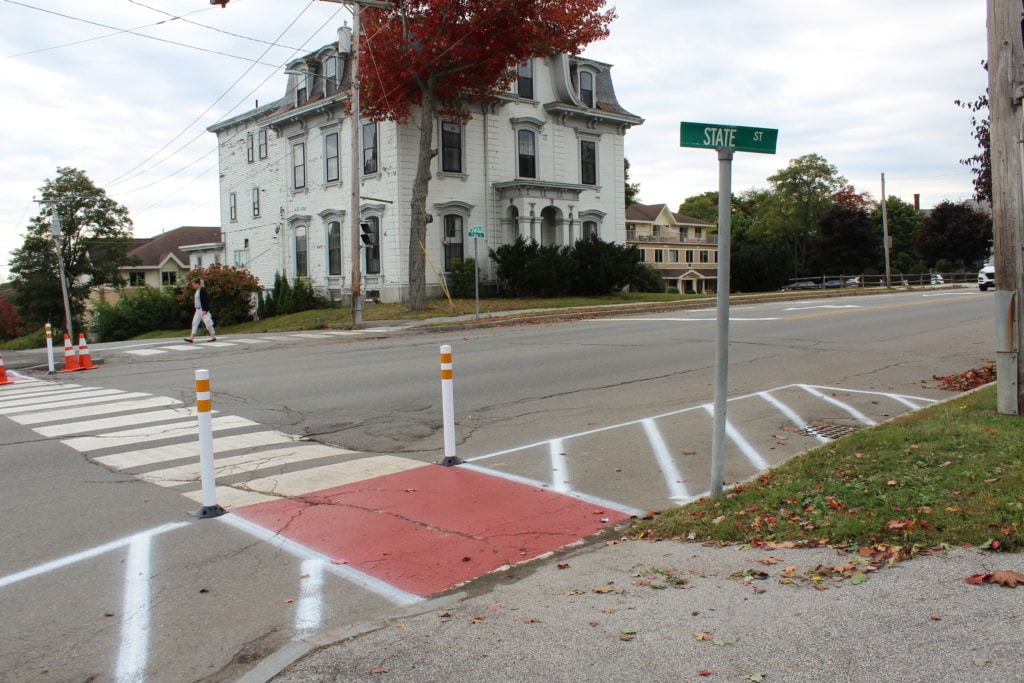 Crosswalk enhanced by paint, bollards, and no parking zones.